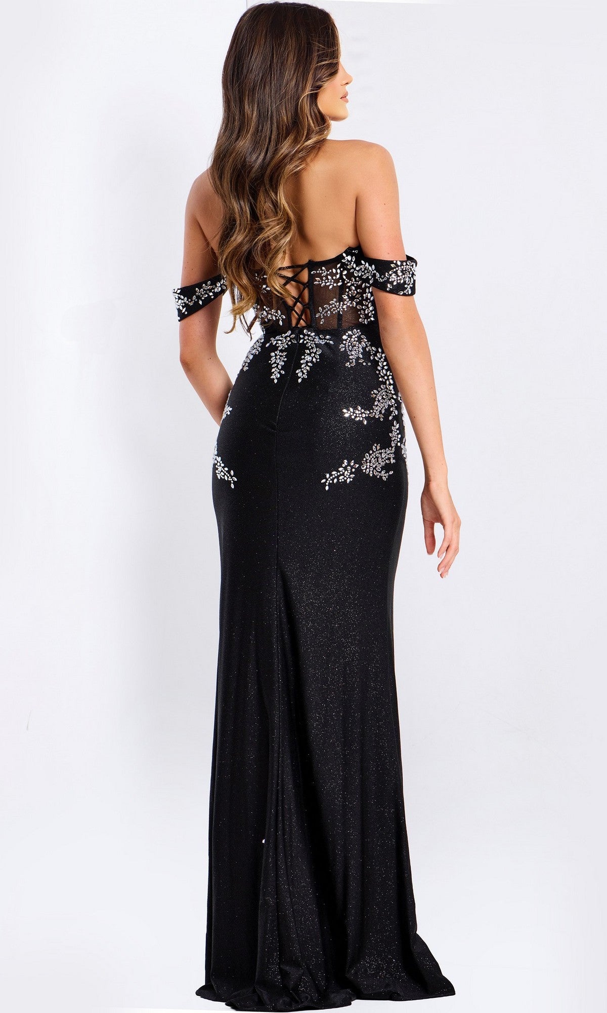 A woman in the Jovani 49659 long black prom dress with off-the-shoulder sleeves, silver beaded appliques, and a lace-up back stands facing away from the camera.
